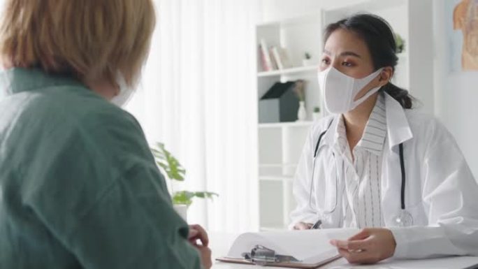 年轻的亚洲女士医生戴防护口罩使用剪贴板正在与医院的女孩患者讨论结果或症状发表重大新闻谈话。