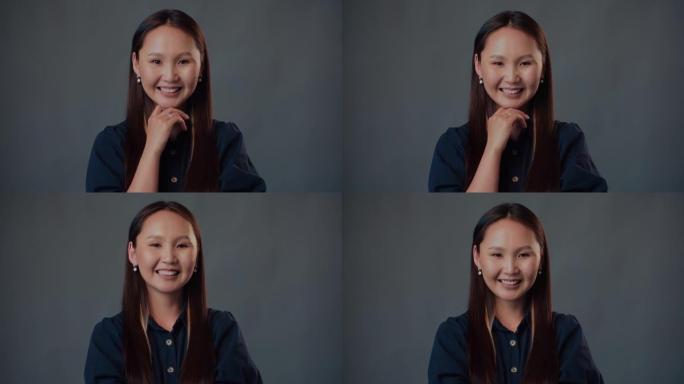 年轻聪明快乐的亚洲女商人的特写肖像对着镜头微笑，触摸着孤立在灰色背景下的下巴。