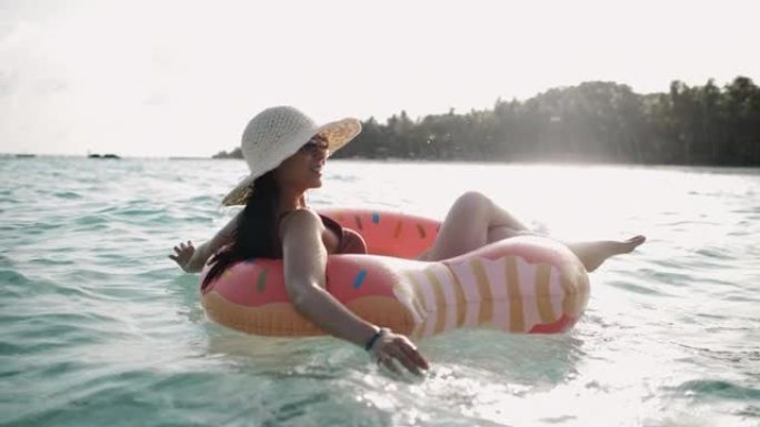 亚洲妇女漂浮在海中的橡胶圈中，在海滩上度假