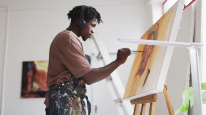 非裔美国男艺术家戴着耳机在艺术工作室的画布上绘画