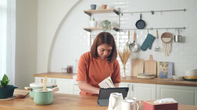 女人在家里的厨房里用数字平板电脑做饭和学习