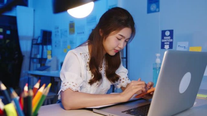 自由亚洲女士在新的普通家庭办公室使用电话努力工作。晚上在房子里超负荷工作。