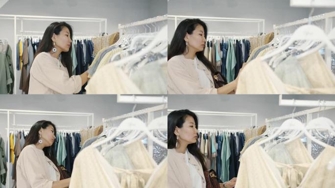 年轻的亚洲女士在现代商店里买衣服的慢动作触摸衣架上的衣服