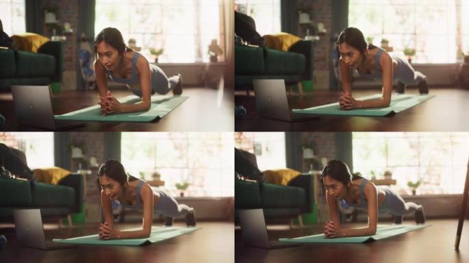 强壮美丽的亚洲健身女孩在锻炼中使用笔记本电脑进行在线锻炼，在家做木板瑜伽锻炼。锻炼服务应用程序，流媒