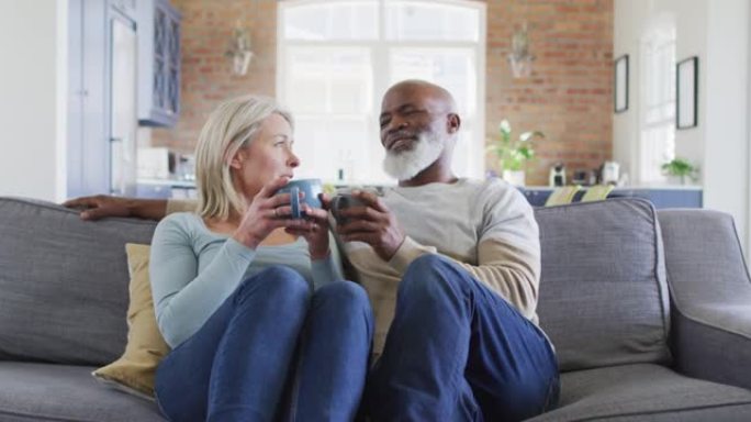 混血高级夫妇坐在家里的沙发上一起喝咖啡