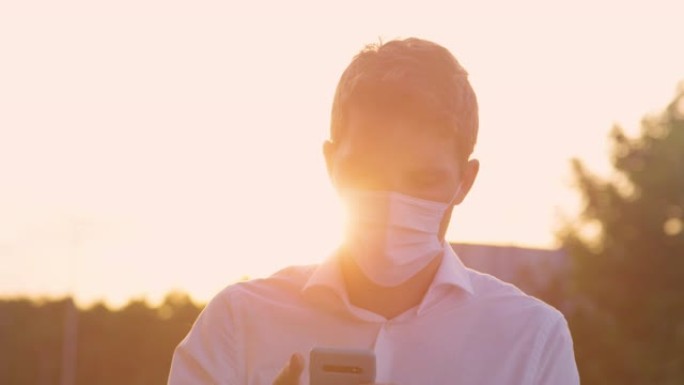 特写: 在一个阳光明媚的夏日傍晚，戴着医用口罩的年轻人发短信。