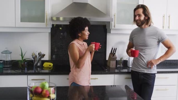 混血夫妇拿着咖啡杯在家里的厨房里互相交谈