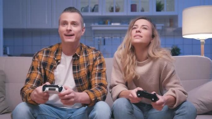 动作游戏玩家年轻的男人和女人坐在沙发上，在数字控制台上玩视频游戏。两名玩家在控制视频游戏操纵杆中玩游