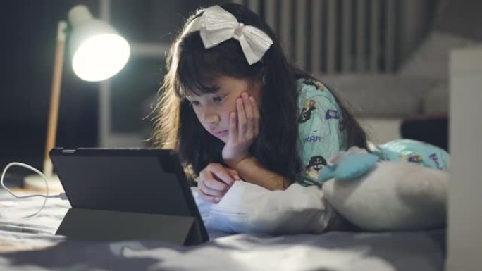 小女孩晚上在卧室玩数字平板电脑在线学习