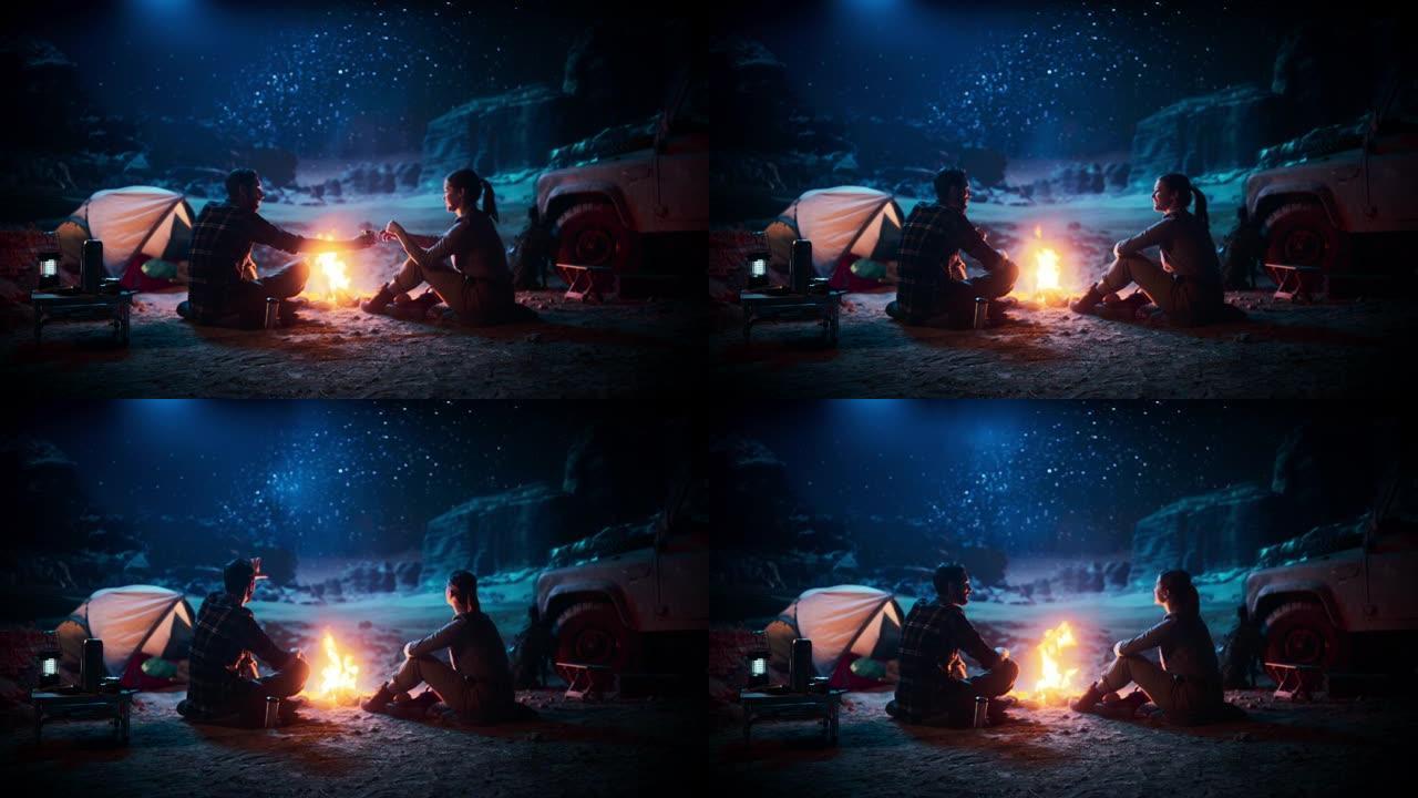 快乐的夫妇坐在篝火旁，在峡谷露营时看着夜空。两个旅行的人在露营地讲鼓舞人心的故事，看看银河系的星星。