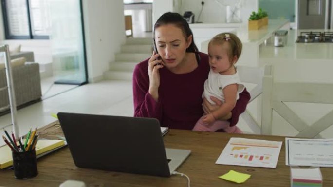 白人母亲在家工作时抱着婴儿并在智能手机上聊天