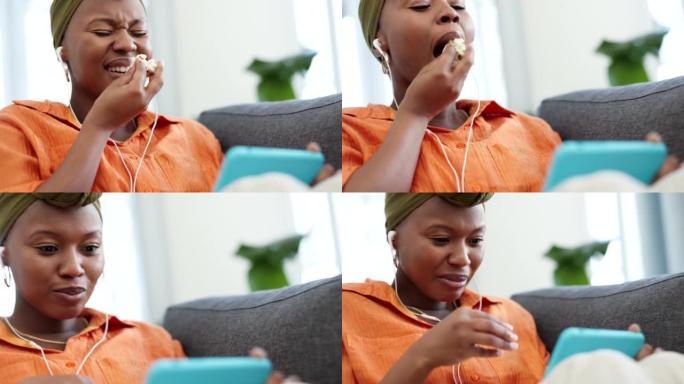 电话流媒体，电影和来自尼日利亚的爆米花女人在沙发上大笑。快乐女性吃食物使用移动技术在家在房子客厅沙发