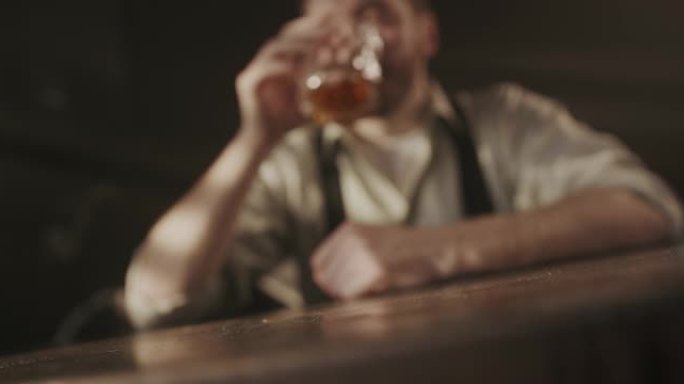 一段视频，视频的前景是一杯威士忌，一个男人拿了一杯饮料，然后把它放回他面前的桌子上