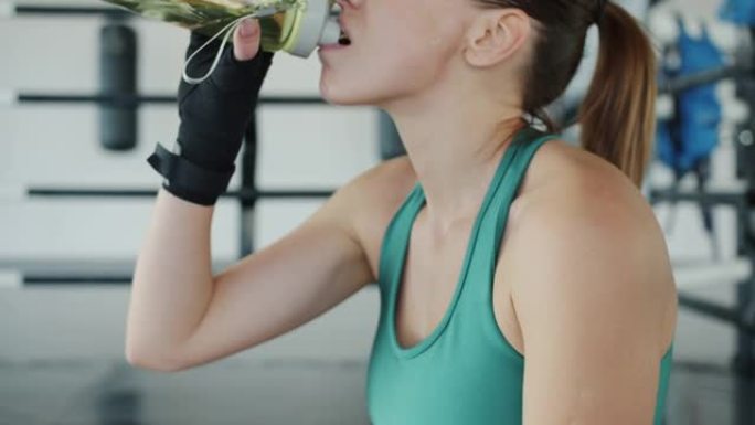 现代体育馆休息时年轻女拳击手喝水的慢动作