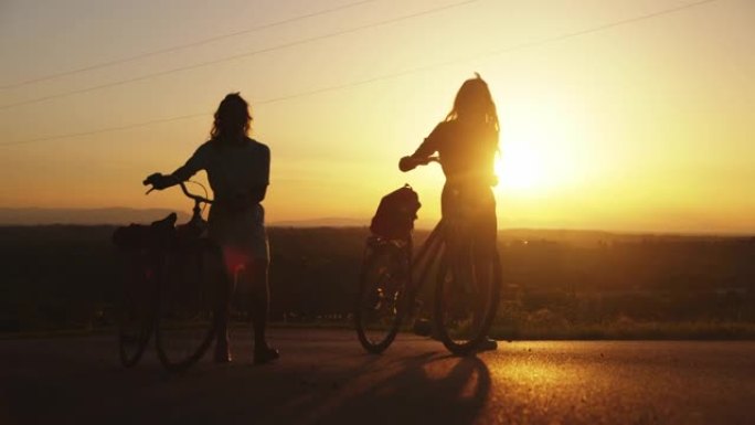 两个女性朋友在路上骑自行车散步的剪影