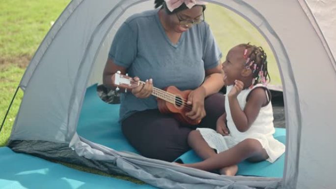 SLO MO快乐的妈妈和她的女儿在公园的帐篷里弹吉他尤克里里琴