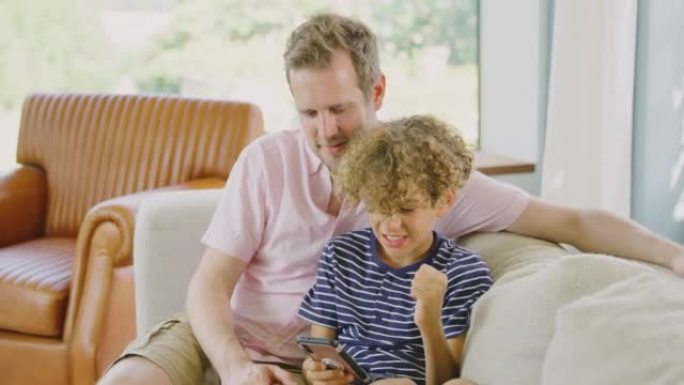 父子俩坐在家里的沙发上玩手机视频游戏-慢镜头拍摄