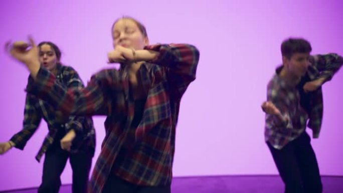 由三名年轻的专业舞者组成的多元化小组，在工作室环境中，在带有深粉色背景的大Led屏幕前近距离表演嘻哈