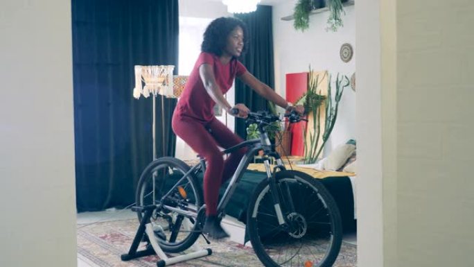 年轻的非洲女士正在禁闭中骑训练自行车