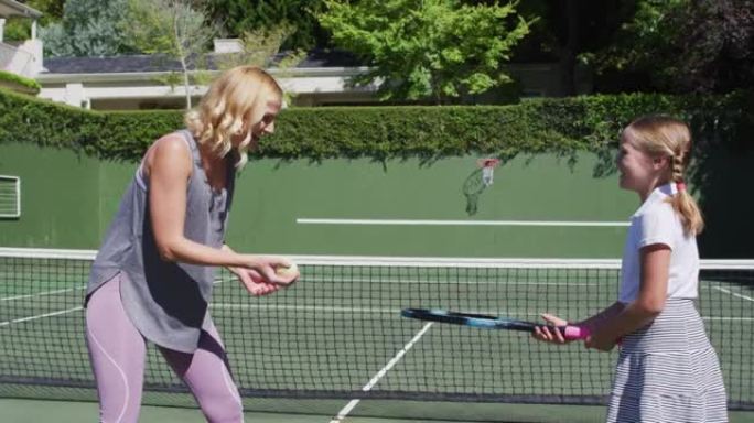 白人母亲在阳光明媚的日子里教女儿在网球场打网球