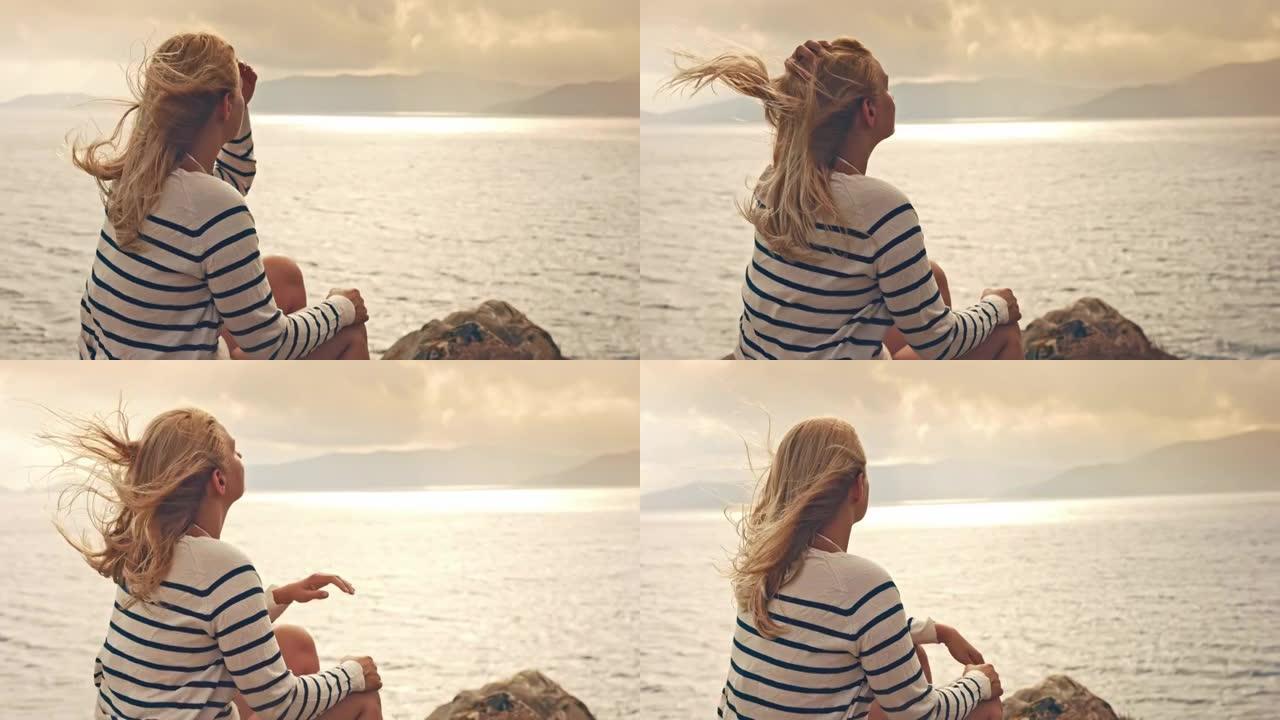一个金发女孩坐在岩石上的景色，撒丁岛。