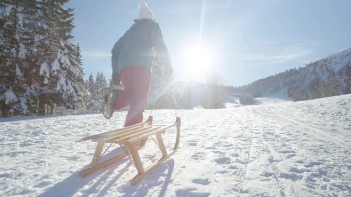 低角度: 无法辨认的年轻女子沿着白雪皑皑的草地奔跑，拉着雪橇