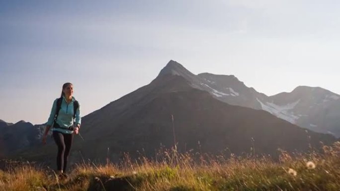 年轻的女徒步旅行者走在被山峰包围的山脊步道上