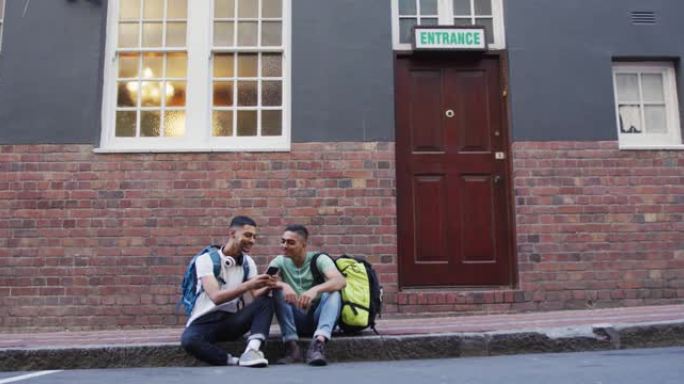 两个混血男性朋友在街上坐着，说话和使用智能手机