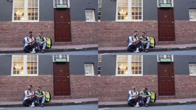 两个混血男性朋友在街上坐着，说话和使用智能手机