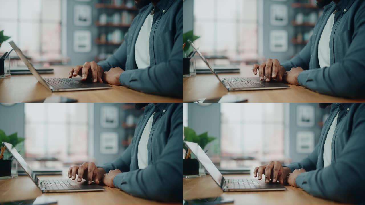 在舒适的客厅坐在桌子后面的时候，一个在笔记本电脑上工作的黑人非洲裔美国人的手关闭。自由职业者在家工作