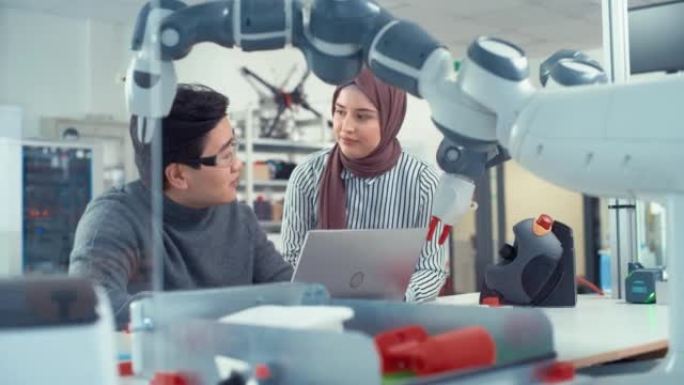在技术研究设施中: 年轻的女性专家与亚洲工程师交谈，他们咨询并指向笔记本电脑屏幕。专业人员致力于自主
