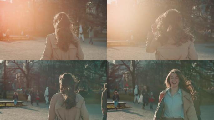 令人惊叹的镜头耀斑拍摄，快乐的年轻女子在阳光明媚的城市公园慢动作中对着镜头微笑。
