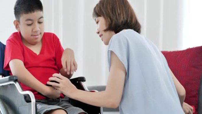 10-11岁的亚洲残疾男孩坐在轮椅上与母亲或护理人员一起在家通过smatphone学习在线课程。残疾