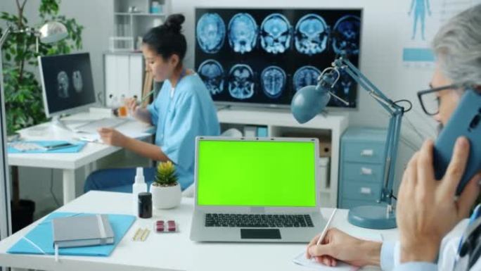 男医生在手机上讨论医学在诊所看绿色色度键笔记本电脑屏幕