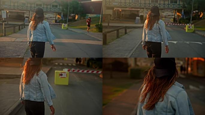 日落时，棕色头发的女人在木板路上的滑板上滑冰，后视图