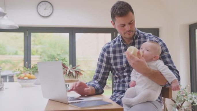在职父亲在家中使用笔记本电脑，同时用奶瓶喂养膝盖上的婴儿儿子