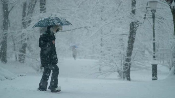 慢动作: 穿着冬衣和背着雨伞的女人在暴风雪中行走