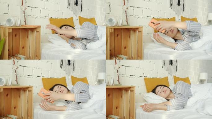 亚洲妇女在床上醒来触摸智能手机屏幕并微笑着在家享受早晨的肖像