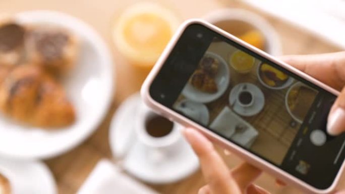 年轻女性游客的俯视图特写镜头，在假期期间，她在一家豪华酒店的智能手机上拍摄完美供应的早餐。