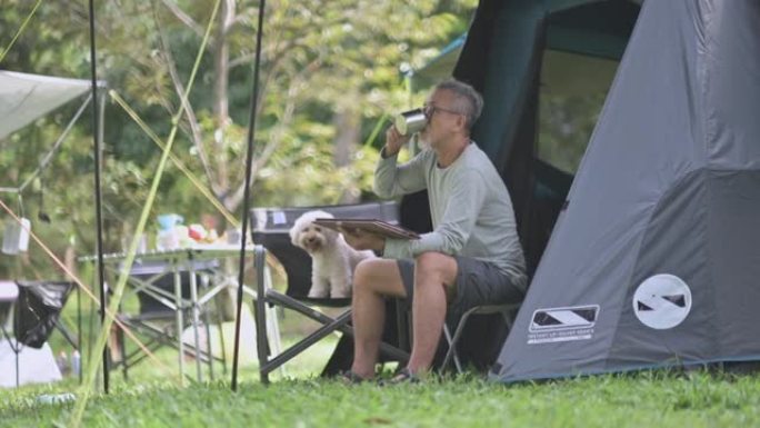 亚洲中国高级男子早上和他的玩具贵宾犬伴侣在野营椅上使用数字平板电脑