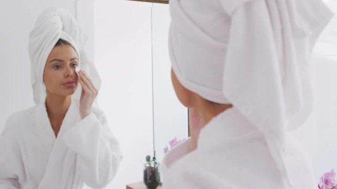 穿着浴袍的女人在照镜子时用棉垫卸妆