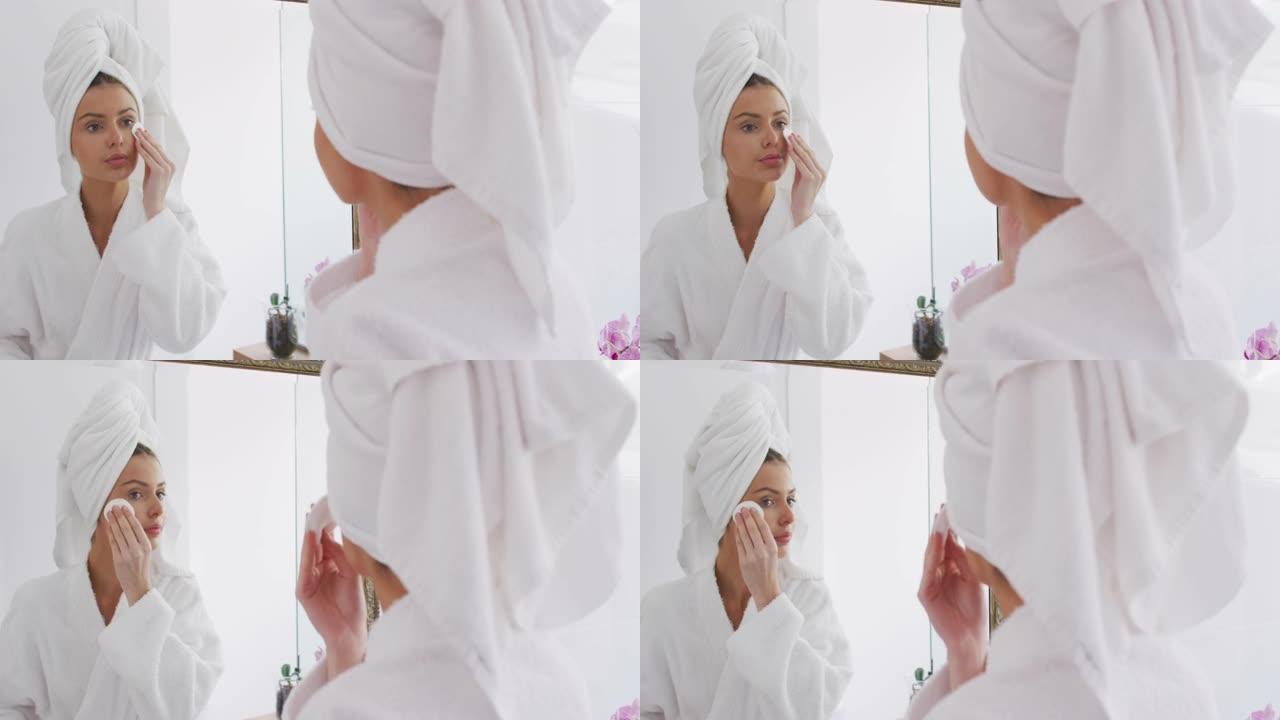 穿着浴袍的女人在照镜子时用棉垫卸妆