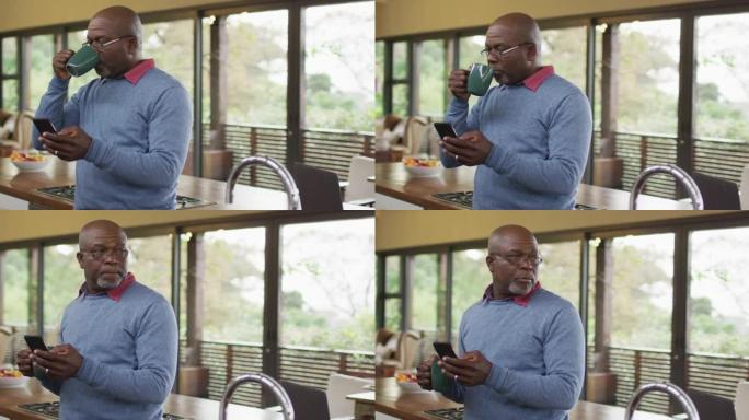 非裔美国高级男子在厨房的柜台上使用智能手机和喝咖啡，将目光移开