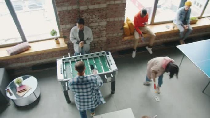 快乐的年轻人在上班休息时放松身心，在办公室打乒乓球和桌上足球