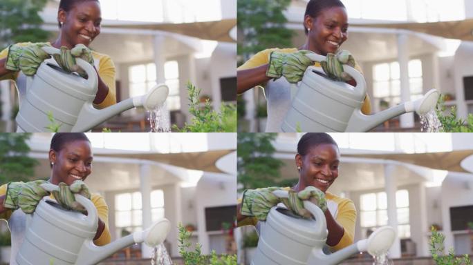 快乐的非洲裔美国妇女戴着手套在花园里浇花