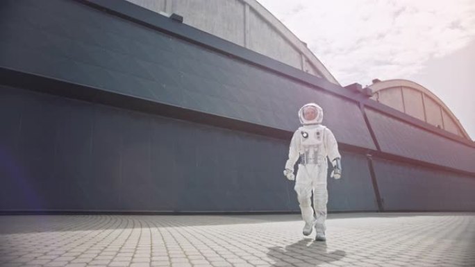 一位自信英俊的宇航员的低角度镜头正从工业金属墙走向相机。明亮的色彩校正。穿着未来派西装的人，手上有技