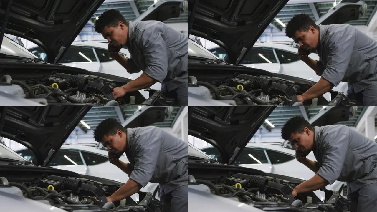 非裔美国男性汽车修理工看着打开的汽车发动机，用智能手机聊天