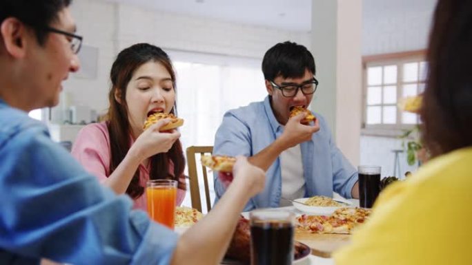 年轻的朋友聚会，一起坐在家里的餐桌旁，吃披萨食物，笑着吃饭。