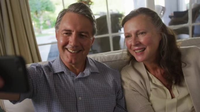 快乐的白人高级夫妇坐在客厅微笑着自拍