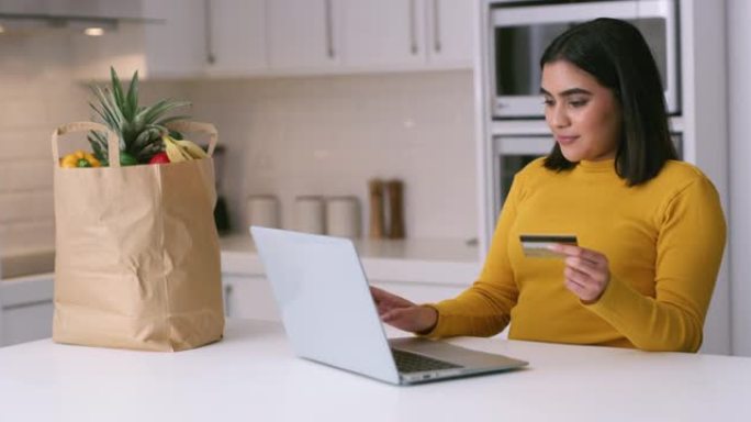 4k视频片段，一名年轻女子在家里的厨房里使用笔记本电脑和信用卡